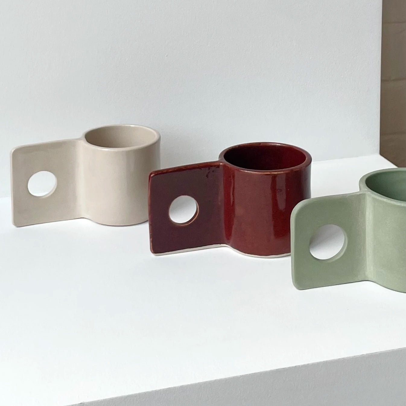 A white background with from left to right the Hopper Mug in sand, burgundy and pistachio green