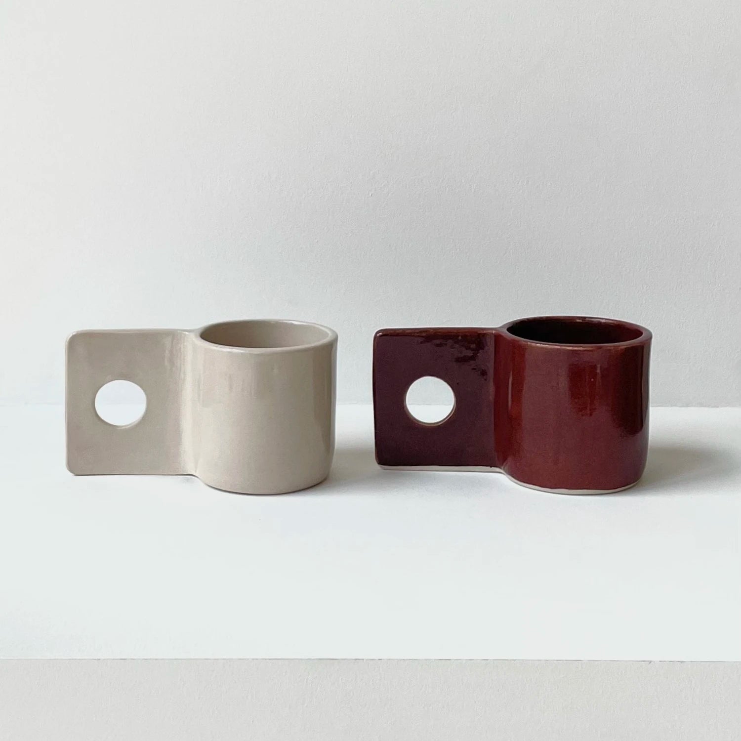 Brutes Ceramics Hopper mugs in sand and burgundy sitting on a white surface with a white background