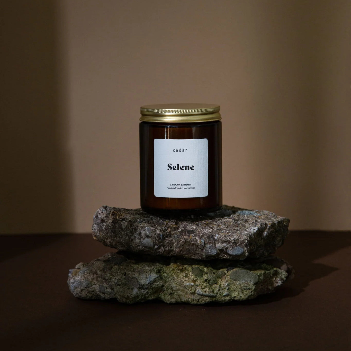 Cedar Lifestyle Selene medium jar candle in a context image sitting atop 2 layers of rock against a brown background
