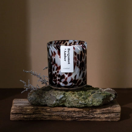 Cedar lifestyles Bergamot and amber candle sitting atop a rock with a sprig of foliage