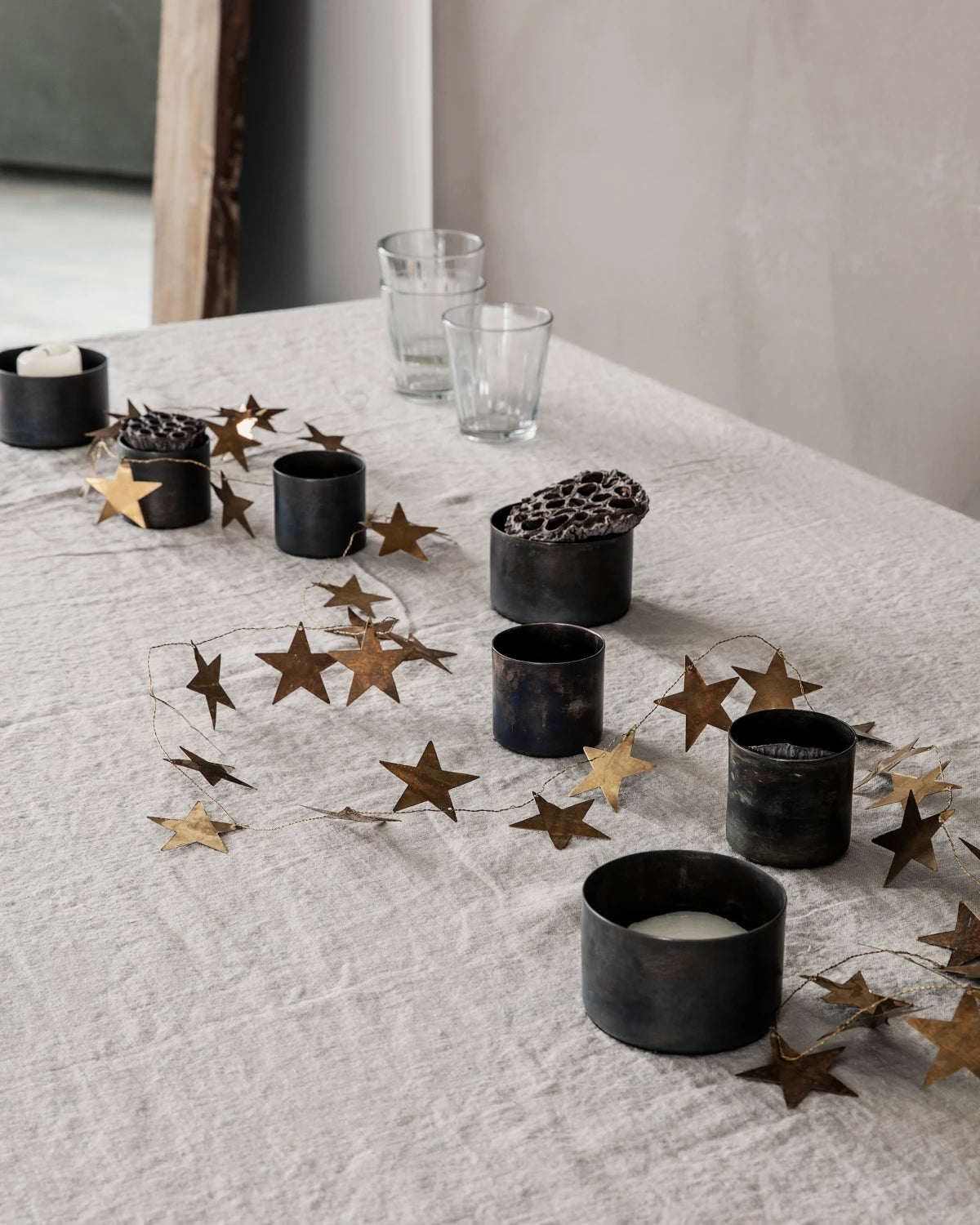 House Doctor antique brass star garland ling across a linen  table cloth with black brass candle holders in between
