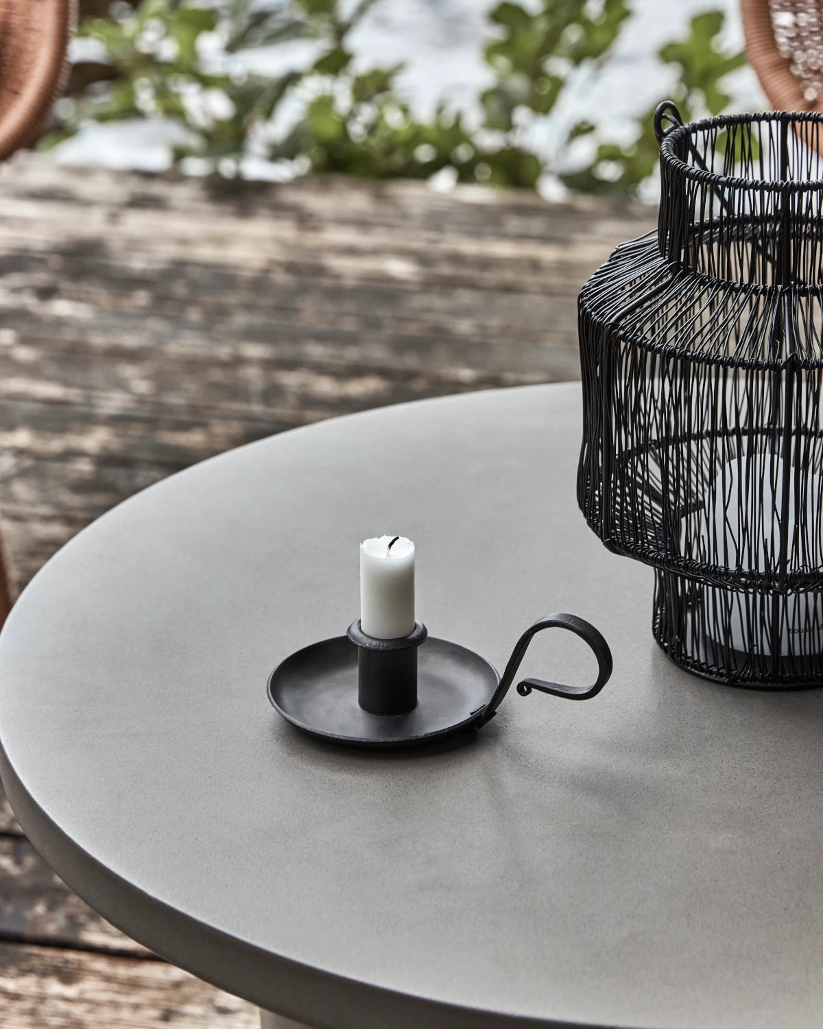 House Doctor Grab Candle Holder in Black Iron sitting on a round grey table outdoors, next to another larger holder