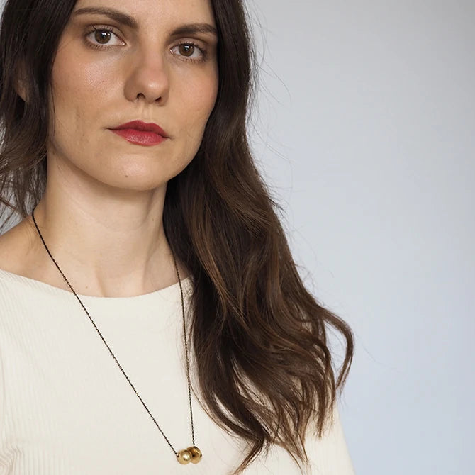 A female model wearing the long Hiku Necklace featuring a heavy brass ball and thick brass disc on a black brass chain by Brass and Bold