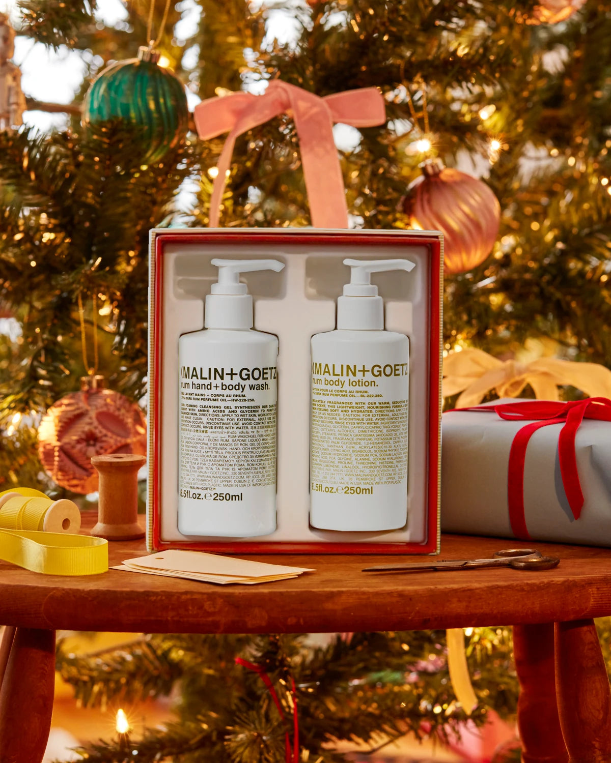 Malin and Goetz Make It A Double Rum Hand and Body gift set standing on a wooden table underneath the Christmas tree