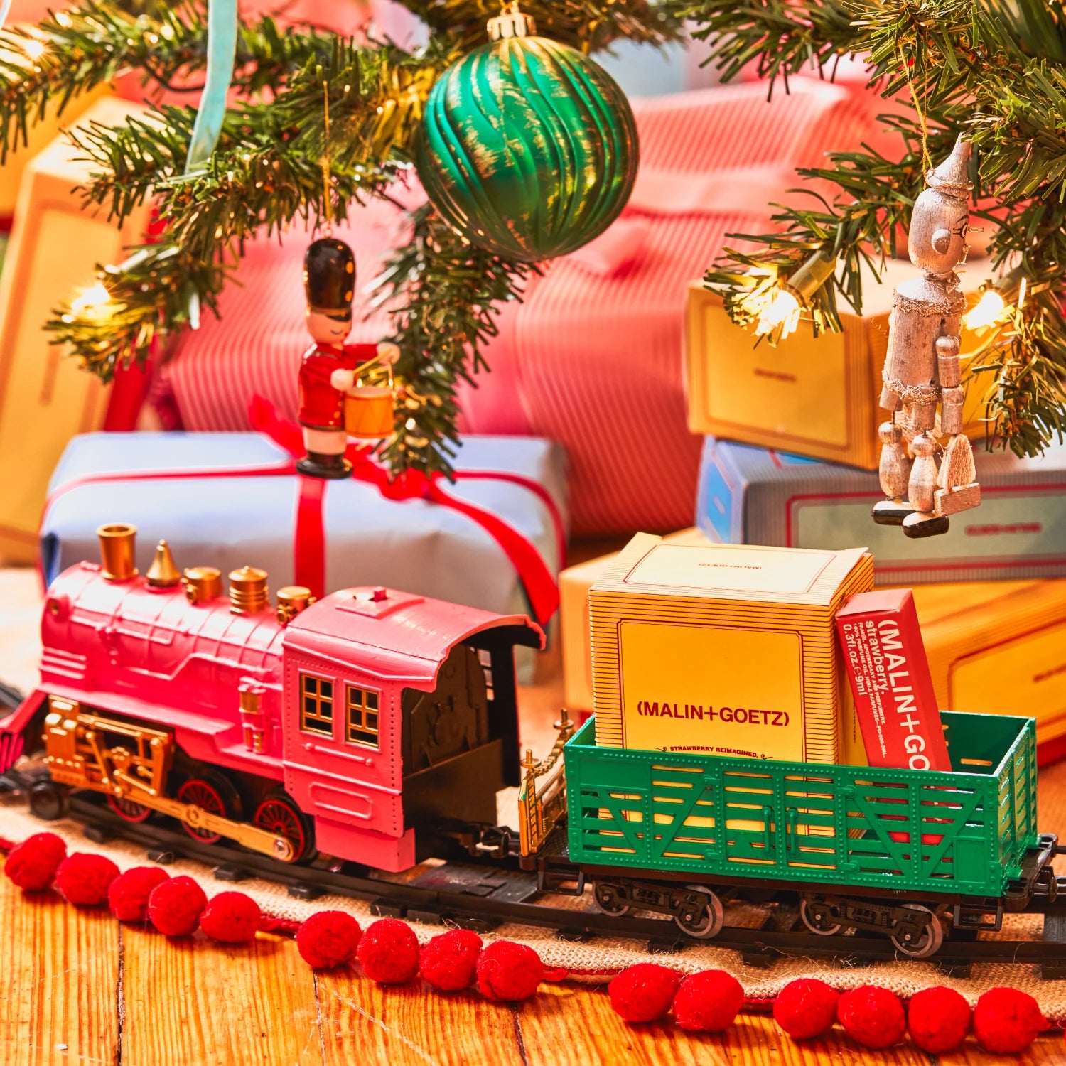 Malin and Goetz Strawberry Reimagined gift set in the carriage of a toy train underneath the christmas tree