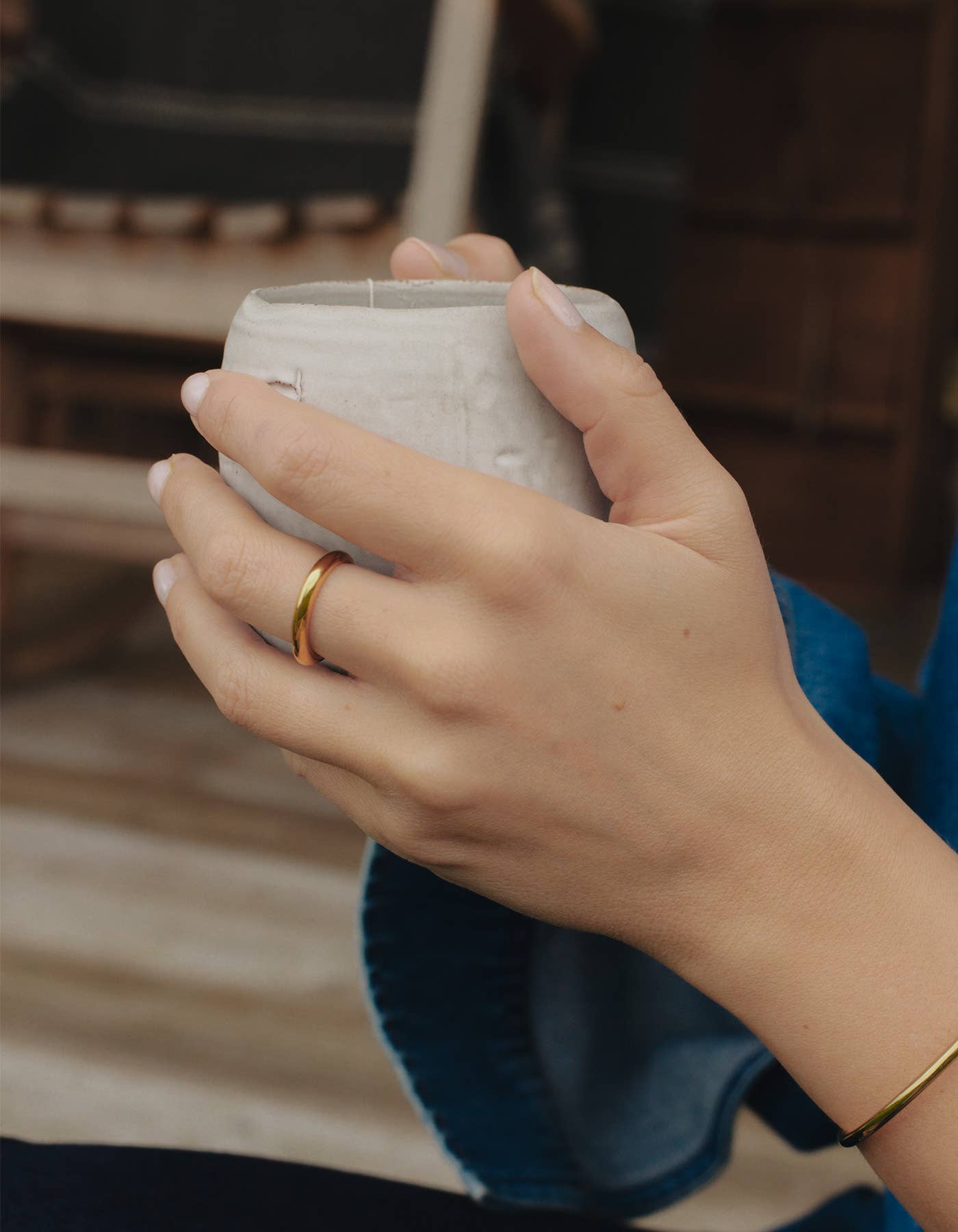 A white persons hand holding a tea cup whilst wearing the gold irregular minimal band ring from Nordic Muse