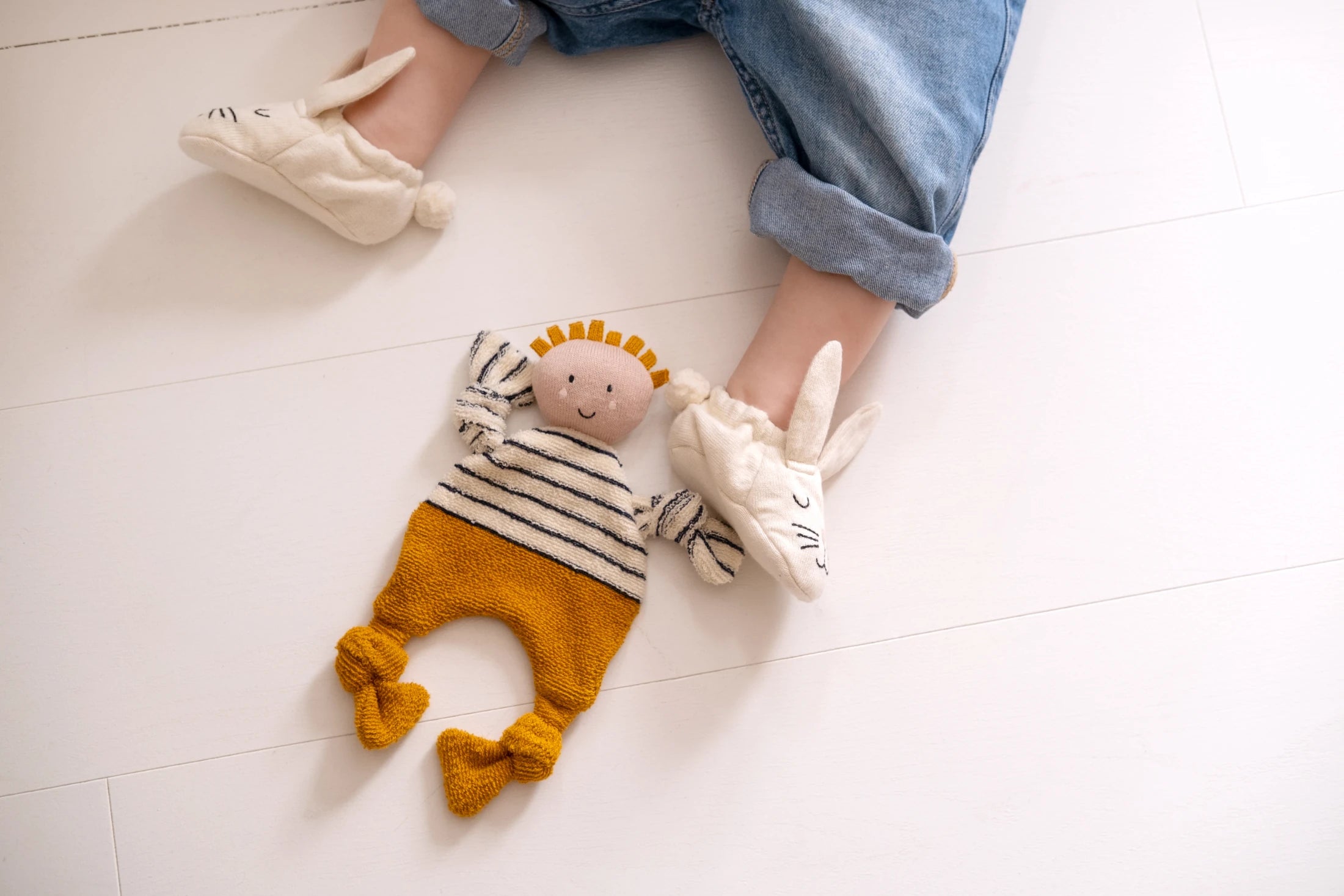 Citrus Buddy Comforter Cuddle Cloth by Sophie Home on a white background next to a baby's feet wearing bunny slippers