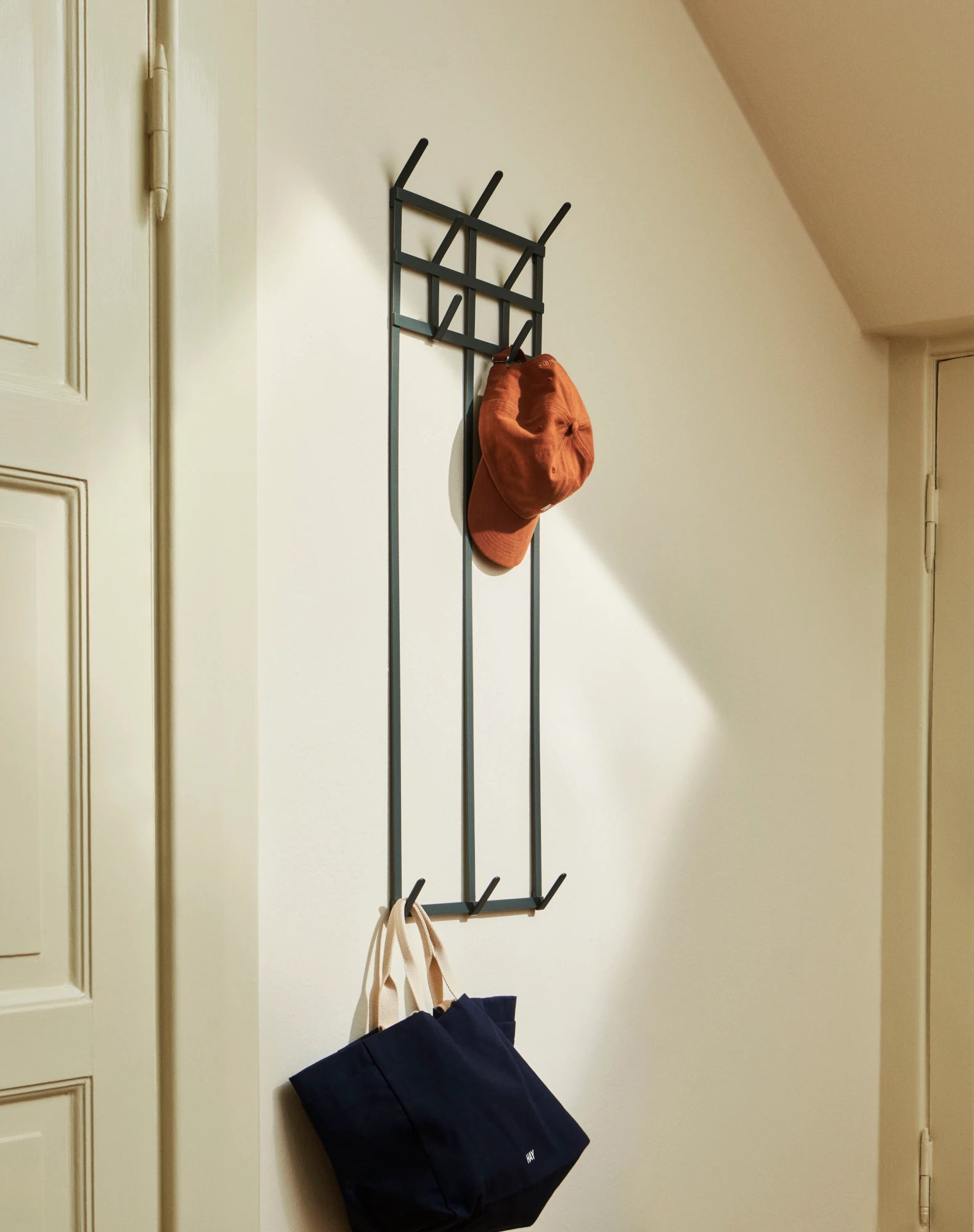 Large Tape Coat Rack in Charcoal by HAY mounted on a wall hanging a bag and a cap | Lifestory