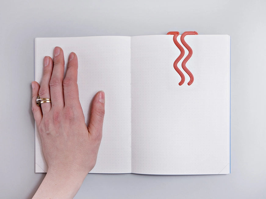 The Completist 3D Printed Miami Bookmark slotted into a plain notebook with a left hand next to it for size reference