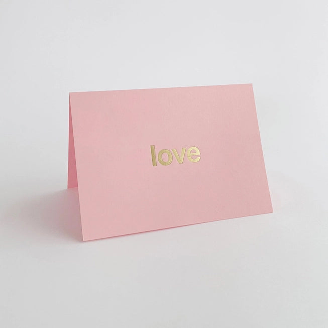 Tom Pigeon brass foiled card with the word love in bold letters on a pink card