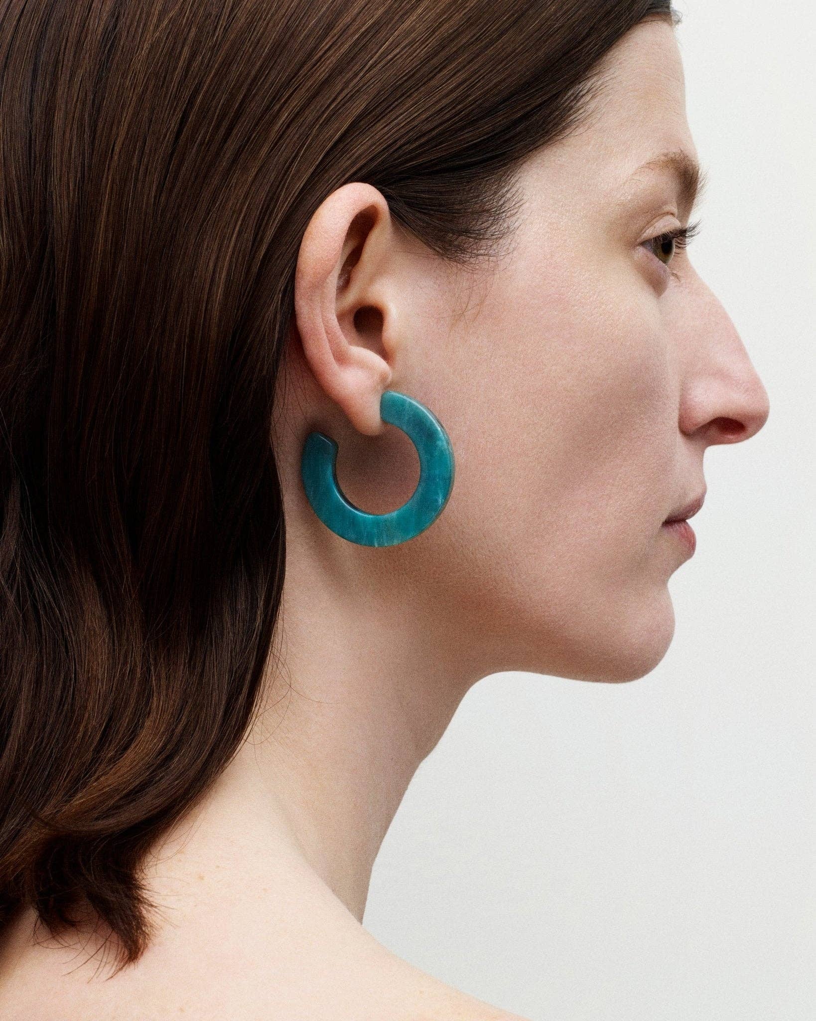 The side profile of a white female model with brown hair wearing MACHETE's Kate hoops in teal