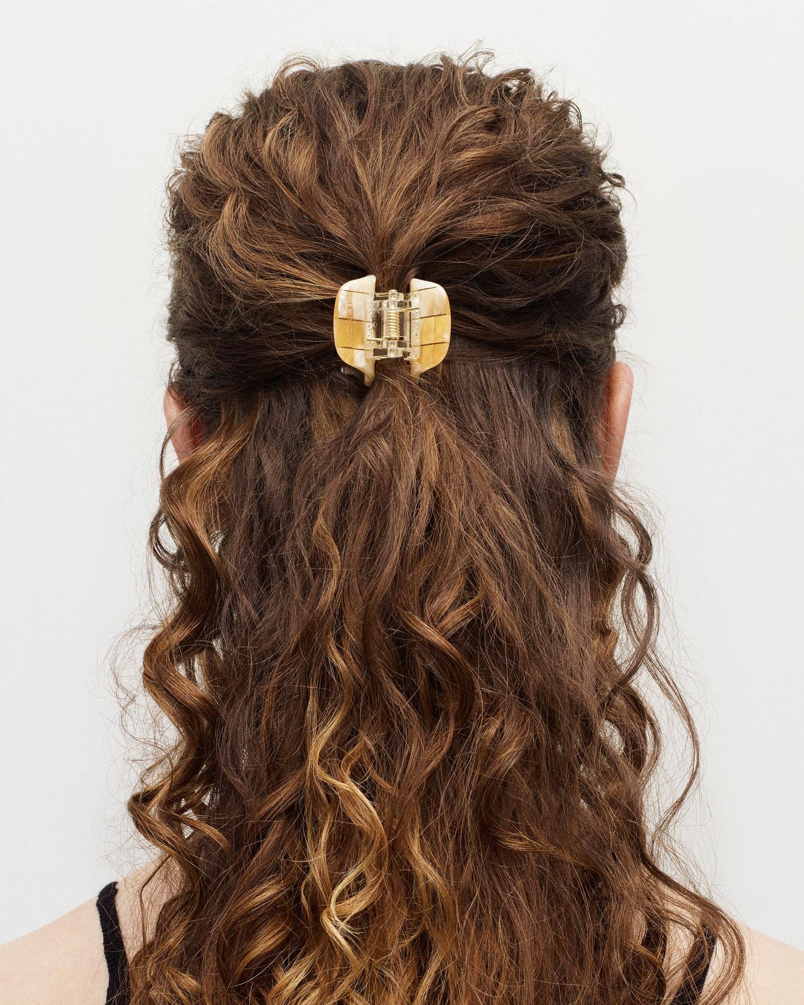 The back view of a white female model with long brown curly hair wearing the MACHETE mini hair claw to keep her hair in a half up style