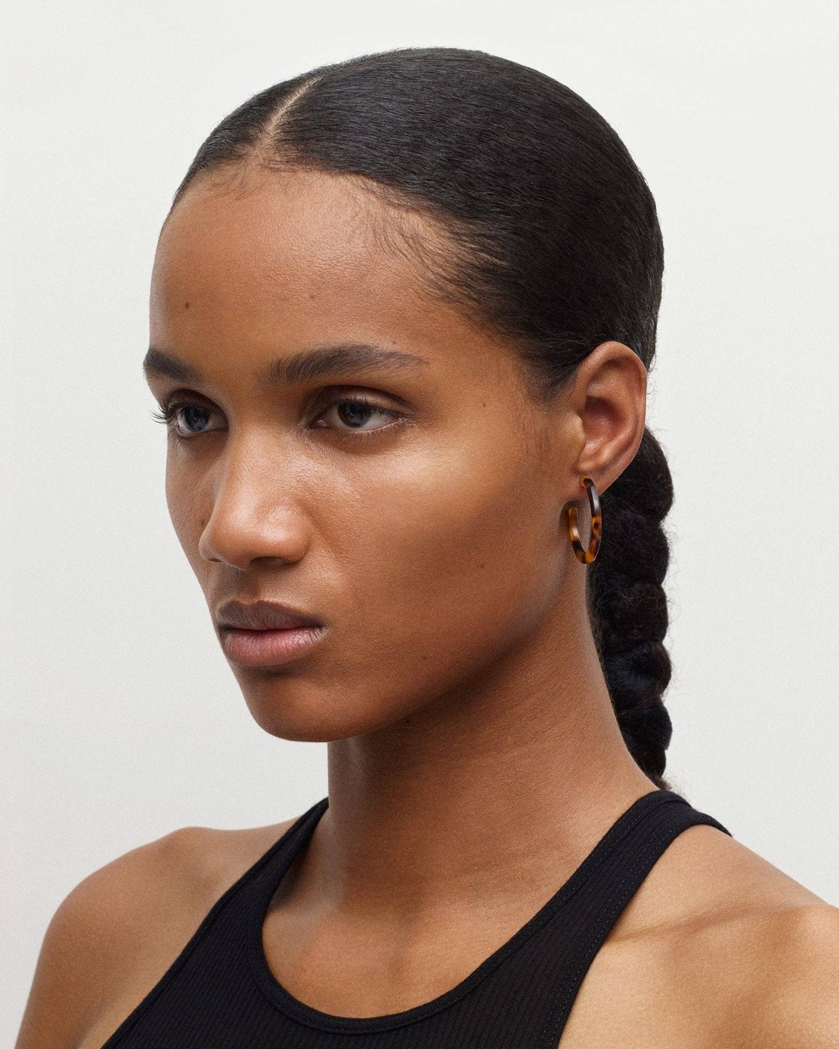 The front side angle profile of a lack female model with her hair tied back in a plait wearing the MACHETE mini hoops in tortoise blend