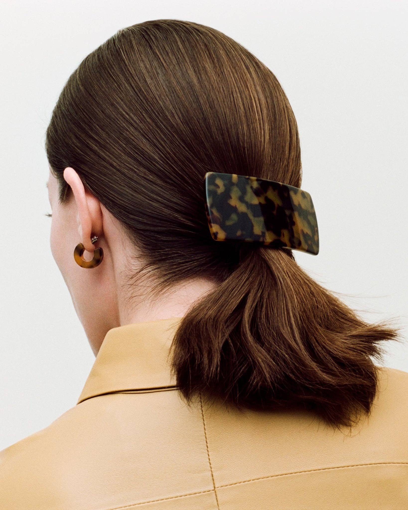 The back side profile of a white female model with brown hair wearing the MACHETE Muse hoops in tortoise with matching hair barrett